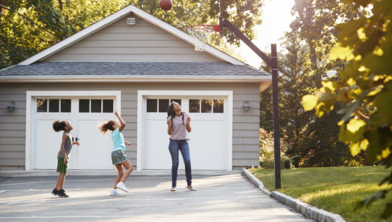 Mother And Children Playing Basketball On Driveway At Home